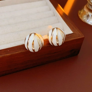 Detailed close-up of gold-plated white enamel round stud earrings on a wooden box