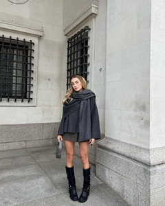 Detailed outdoor view of dark gray knit scarf cape with buckled leather boots and handbag