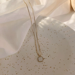 Detailopname van vierkante schelphanger aan een gouden schakelketting op stof