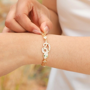 Close-up of gold snake bracelet with white zircons, green gem eyes and heart links