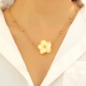 Detail van dubbele gouden ketting met een tropische wit-gele plumeria bloem hanger