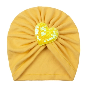 Détail d'un bonnet turban jaune pour bébé avec cœur en paillettes et texture plissée
