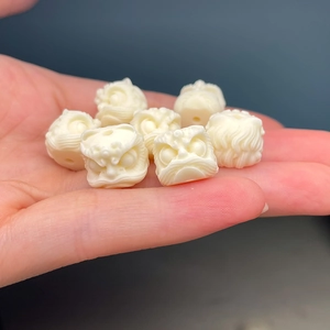 Detailed close-up of white carved lion head beads made of ivory nut on a person palm