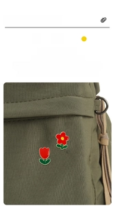 Détail de broches fleur rouge et tulipe en émail fixées sur un sac en toile verte