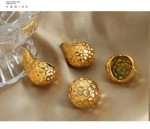Macro detail of golden hammered texture spherical stud earrings on silk fabric