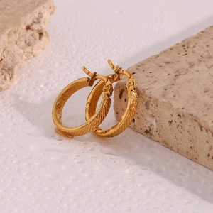 Detail shot of golden striped hoop earrings resting on a stone surface with water droplets