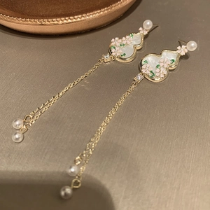 Detail of gold gourd earrings with pink floral accents and pearl tassels in close-up view