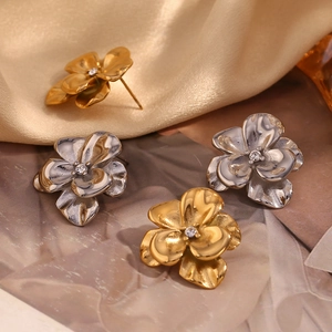 Macro detail of 18K gold floral stud earrings with cubic zirconia on silk background