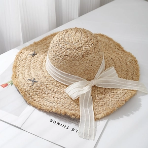 Detail of raffia sun hat with raw edges and an elegant white striped ribbon bow