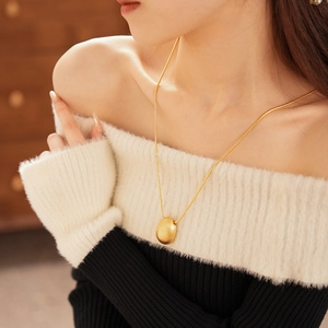 Gros plan d'un pendentif ovale doré sur chaîne serpent porté avec un pull chic à épaules nues