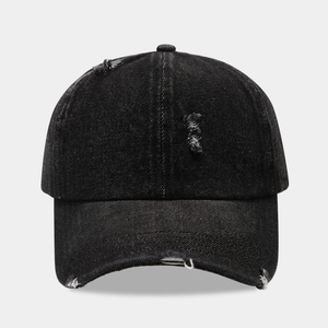 Détail de casquette de baseball en jean noir avec déchirures usées et bords effilochés