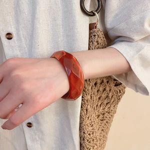 Close-up of geometric faceted amber resin bangle on wrist with summery cotton shirt