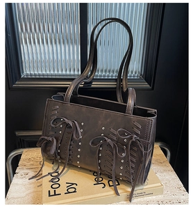 Detail of dark grey PU tote bag featuring woven bow ties and silver metallic rivets