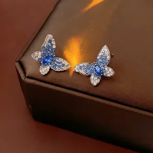 Elegantes pendientes de mariposa con cristales azules sobre un joyero de cuero marrón
