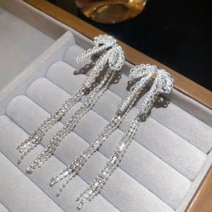 Detailed close-up of silver bowknot tassel earrings with shimmering zircons on velvet