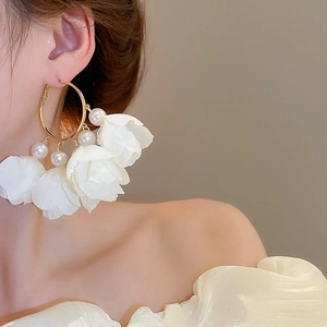 Detailed view of floral tassel earrings with pearls and white fabric petals on large gold hoops