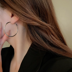 Close-up of a silver minimalist large hoop earring worn by a model in black attire