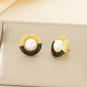 Détail de boucles d'oreilles vintage avec base dorée, perle blanche et résine noire