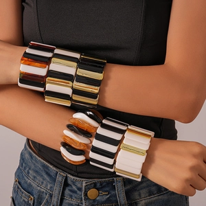Close-up of stacked geometric acrylic elastic bracelets featuring amber and stripe patterns