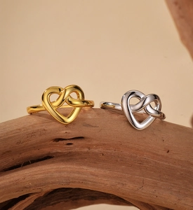Detailed close-up of gold and silver heart knot rings on a textured wooden stand