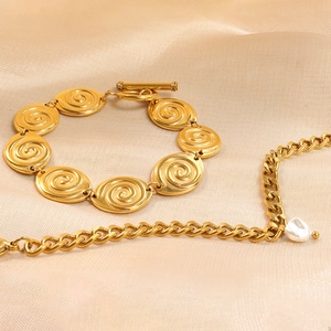 Gold spiral link bracelet with T-bar clasp and baroque pearl charm on beige silk cloth