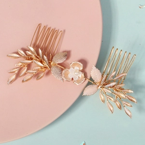 Close-up of golden leaf bridal hair combs with white pearl flowers on a pink tray