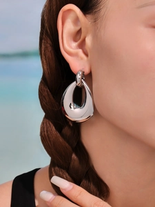 Polished silver metal teardrop earring shown on a model with a scenic beach background