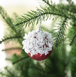 Sparkling red Christmas ball with snowy white flakes hanging on a festive tree branch