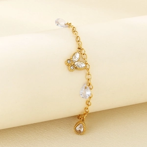Detailed close-up of 18K gold butterfly and teardrop crystal charms on a steel anklet