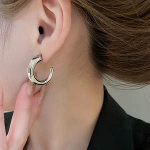 Close-up of minimalist silver C-shaped hoop earrings with a mirror finish on model