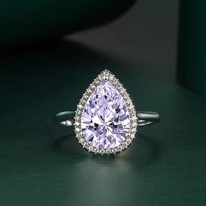 Detailed macro shot of a pear-cut purple zircon ring with silver setting on green background