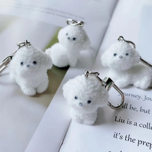 Cute white flocked puppy keychains with soft texture and metal rings on book background