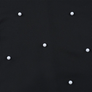 Vue macro du tissu côtelé noir orné d'élégantes perles blanches brodées sur la robe