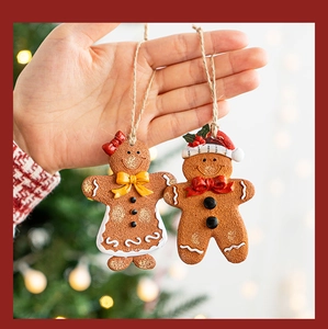 Detail of two gingerbread man Christmas ornaments held against a festive tree background