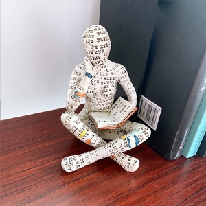 Close-up of reading woman resin sculpture with typography patterns on wooden table