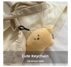 Detail show of yellow croissant plush charm with cute facial embroidery on checkered bag