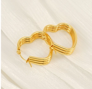 Close-up of triple-layered golden heart hoop earrings on a soft white textured background