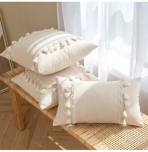 Close-up of beige cotton linen fringe pillows on a woven bench by white curtains