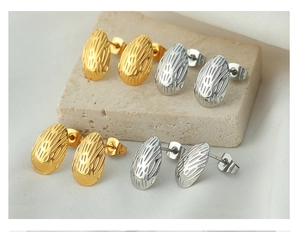 Detailed view of oval titanium steel earrings with textured finish in gold and silver