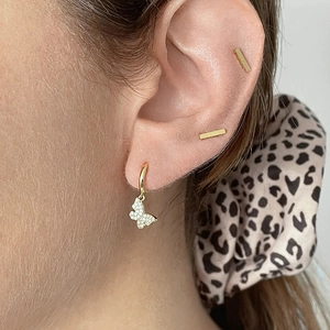 Macro shot of gold butterfly drop earring with white zircon inlay and simple bar studs