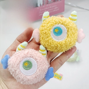 Close-up of cute plush monster pins with embroidered single eye and colorful star wings