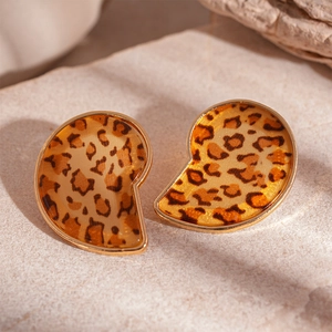 Close-up of golden teardrop earrings with leopard resin inlay on beige stone background