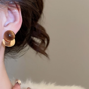 Close-up of a 18k gold bird stud earring with tiger eye stone tassel worn by a model