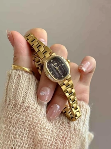 Close-up of elegant gold oval watch with diamond bezel and black checkered dial on wrist