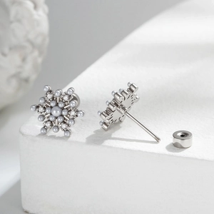 Elegant silver snowflake stud earrings with grey pearls and cubic zirconia on a stone block