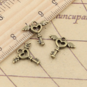 Three antique bronze heart-shaped wing key pendants displayed on a ruler for size