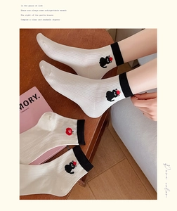 Close-up of white cotton socks with black cat and red apple embroidery detail