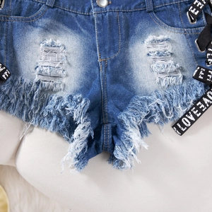 Dettaglio di pantaloncini in denim strappati con nastri neri con scritta LOVE laterale