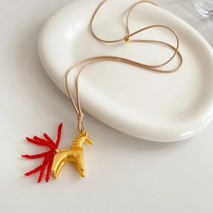 Détail d'un pendentif cheval doré avec queue en perles rouges sur cordon ciré beige