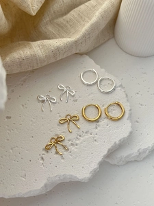 Detailed display of silver and gold bow tassel earrings and minimalist round ear buckles